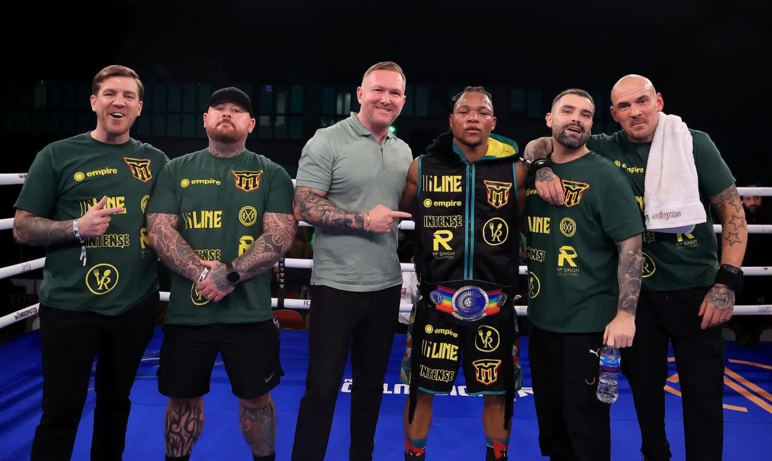 Boxer wearing a championship belt with the team in green Intense shirts in the ring
